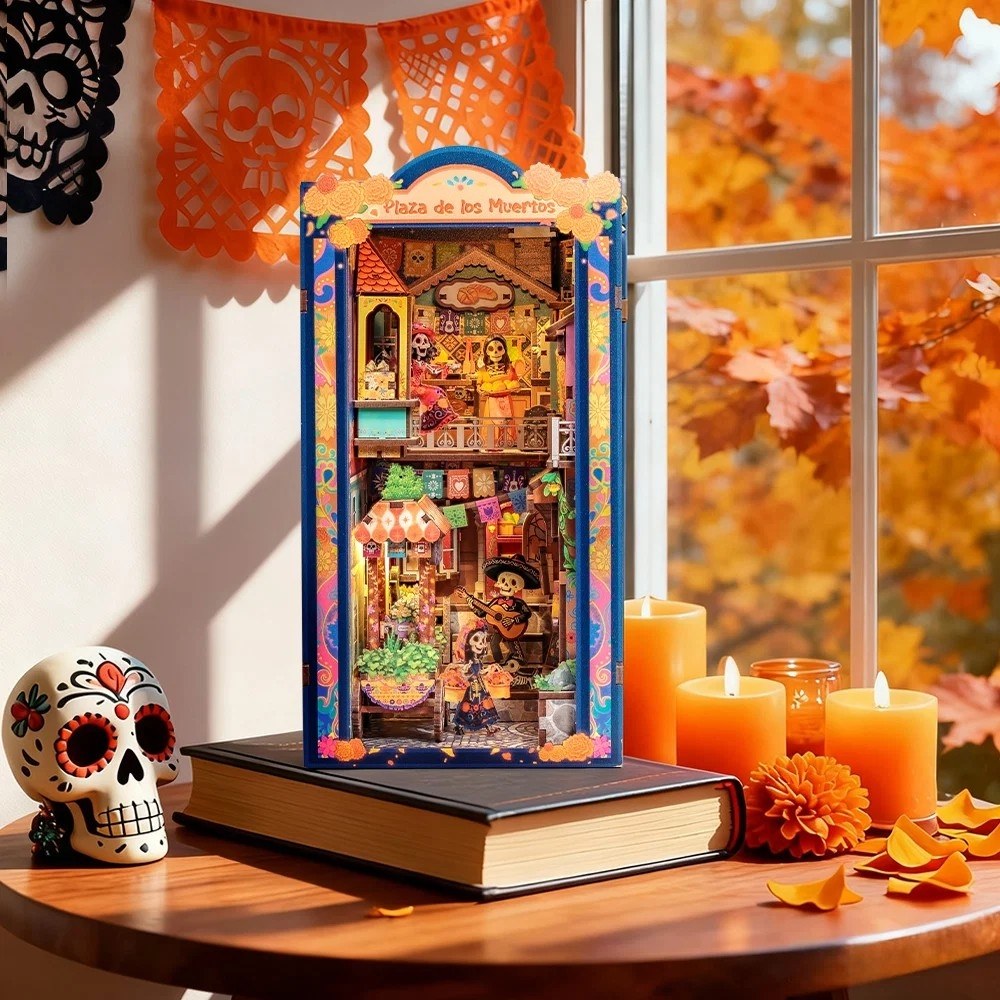 Decorative miniature book nook with a colorful Halloween-themed lantern, candles, and a sugar skull on a table.
