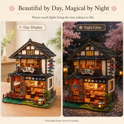 A decorative miniature house model shown in a side-by-side comparison labeled 'Day Display' and 'Night Glow.' The left panel shows the house lit during the day with warm interior lights and a light wood background; the right panel shows the same house glowing at night with pink cherry blossoms and warm orange light.