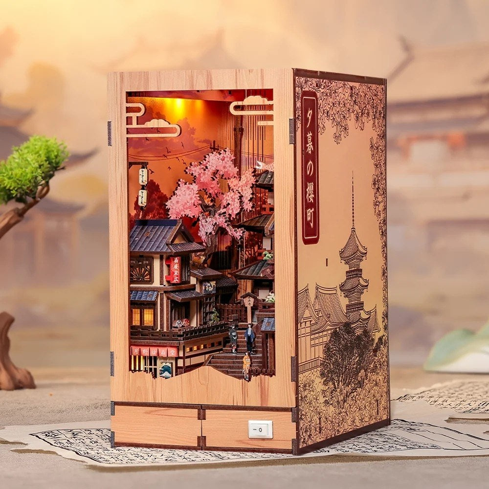 Wooden miniature model of a Japanese temple with cherry blossoms and traditional architecture inside, on a blurred landscape background.