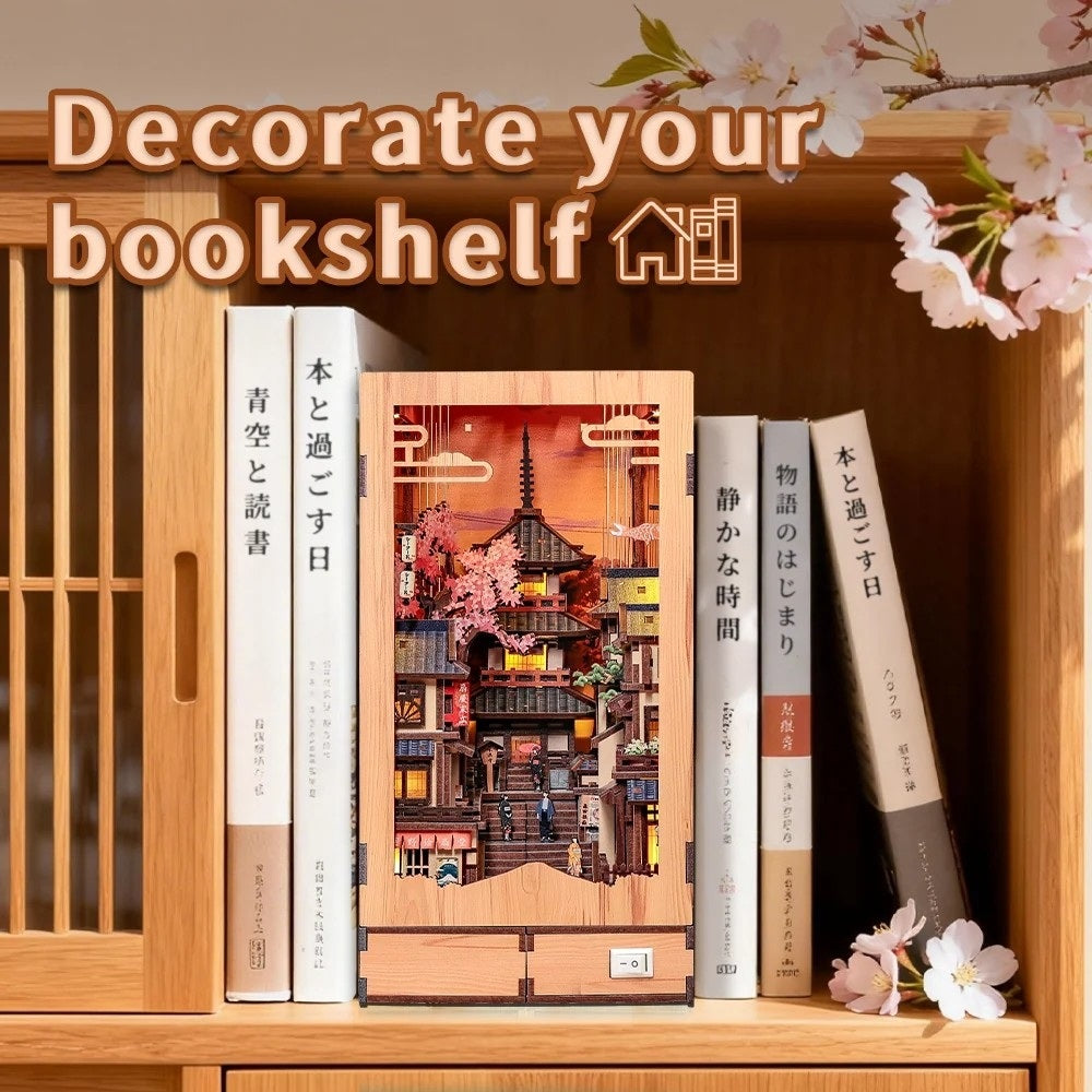 Decorative bookend with a Japanese cityscape design on a bookshelf with books and cherry blossoms.
