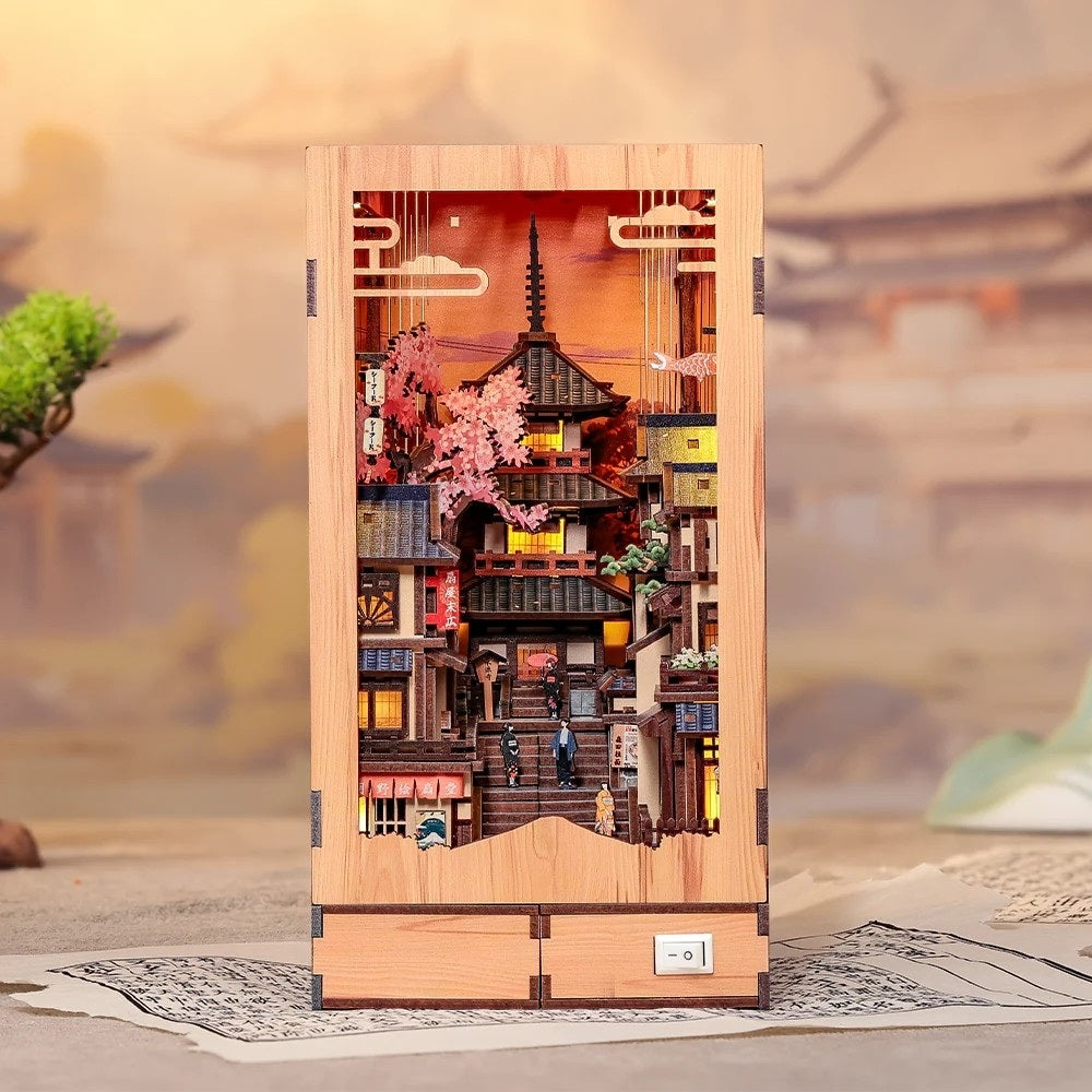 Wooden model of a traditional Japanese village with cherry blossoms and pagoda, set against a blurred landscape.