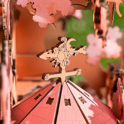 Close-up of a decorative wooden weather vane with intricate carvings and pink cherry blossoms in the background.