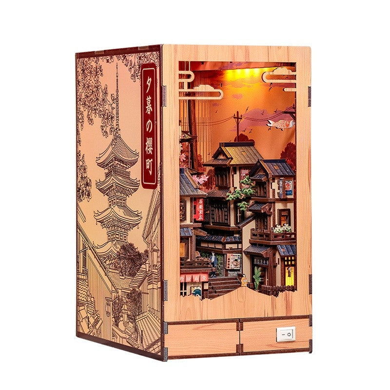 A wooden Japanese-style book nook kit box with a detailed illuminated diorama of traditional houses and a pagoda on the front, shown on a plain white background.