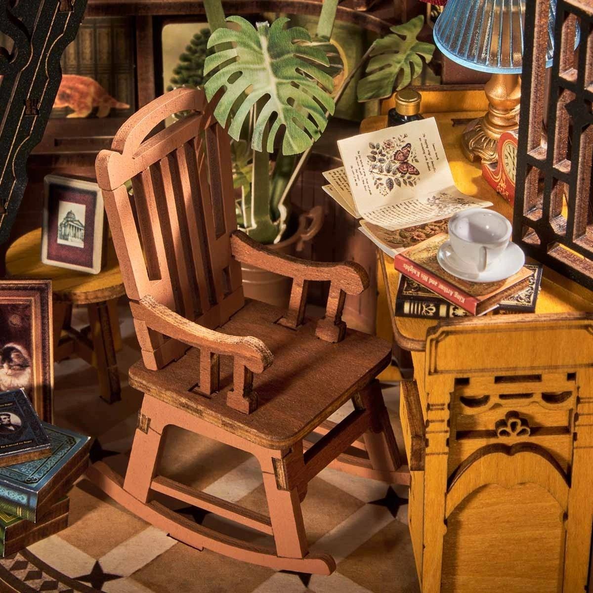 Wooden miniature rocking chair in a miniature room setting with books and plants.