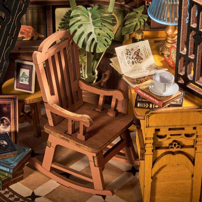 Wooden miniature rocking chair in a miniature room setting with books and plants.