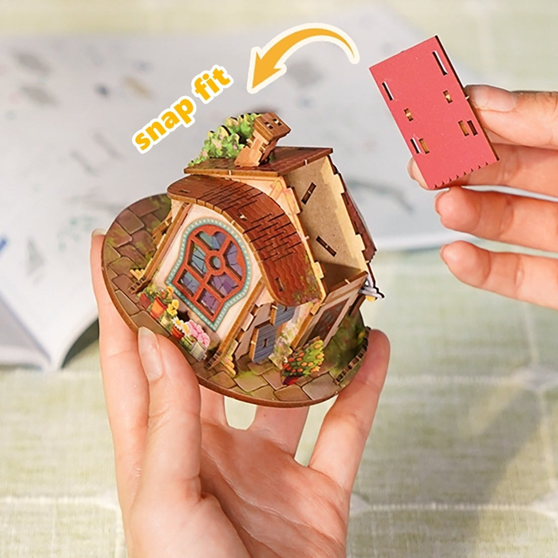 Miniature house model with a hand holding a red component labeled 'snap fit'.