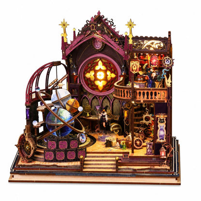 A highly detailed celestial-themed wooden model kit displayed on a clean white background. The intricate miniature structure features a multi-level house with a glowing central window, a large brass-style armillary sphere, gears, gears, and tiny figurines.