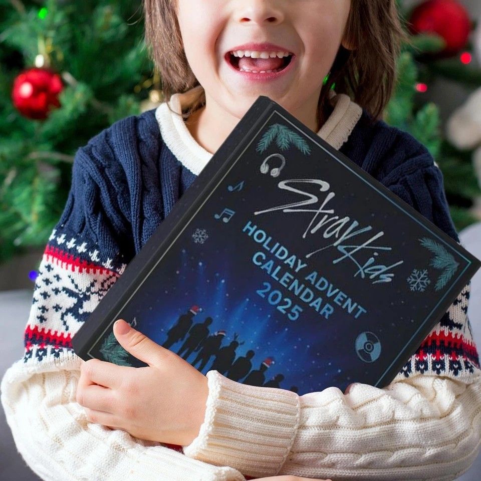 Child holding a 'Holiday Advent Calendar 2025' in front of a Christmas tree.
