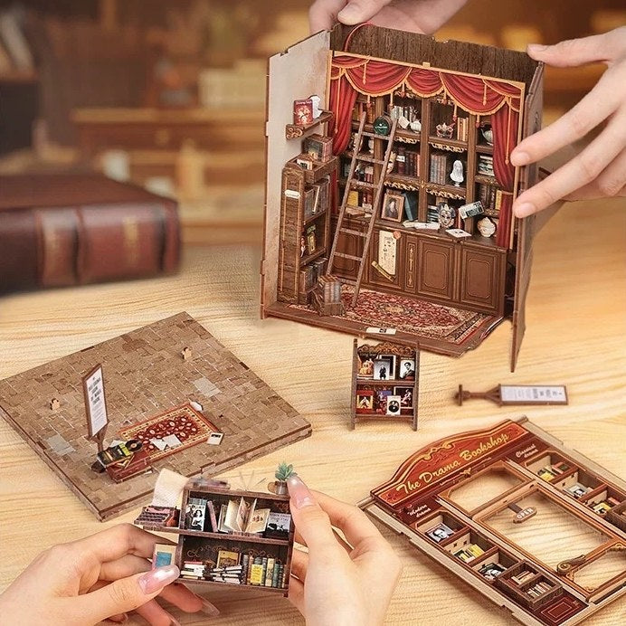 Miniature book nook with a detailed interior scene, held open by hands on a wooden surface.