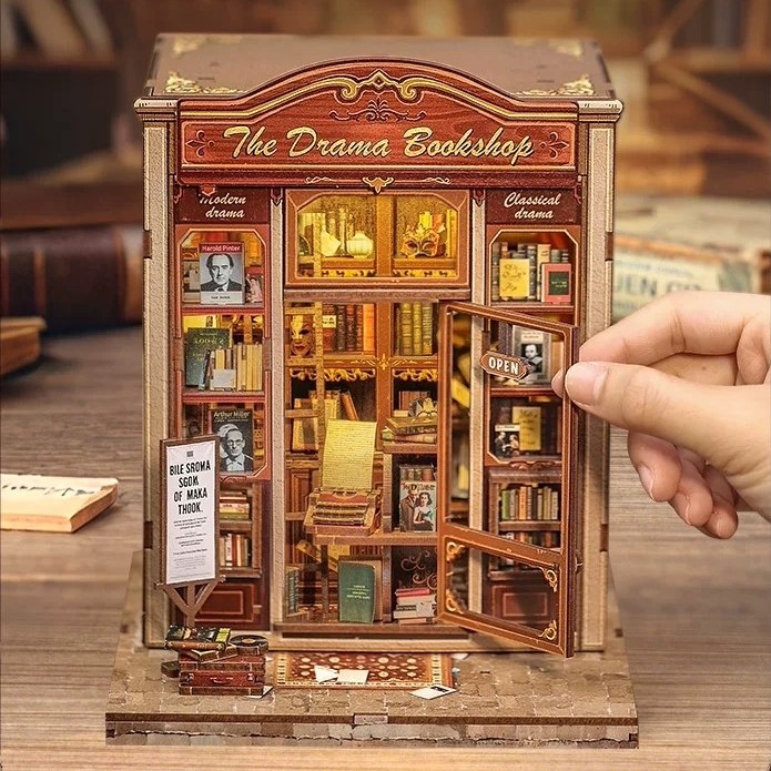 Miniature model of 'The Drama Bookshop' with books inside and a hand opening a door.
