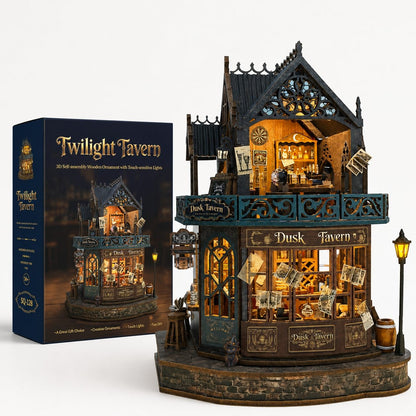 Twilight Tavern wooden miniature set shown with its retail box on a clean white background. The assembled ornament is a detailed two-story pub structure with warm glowing windows, dark teal and brown wood tones, decorative signage, and small included accessories like a street lamp and barrels.