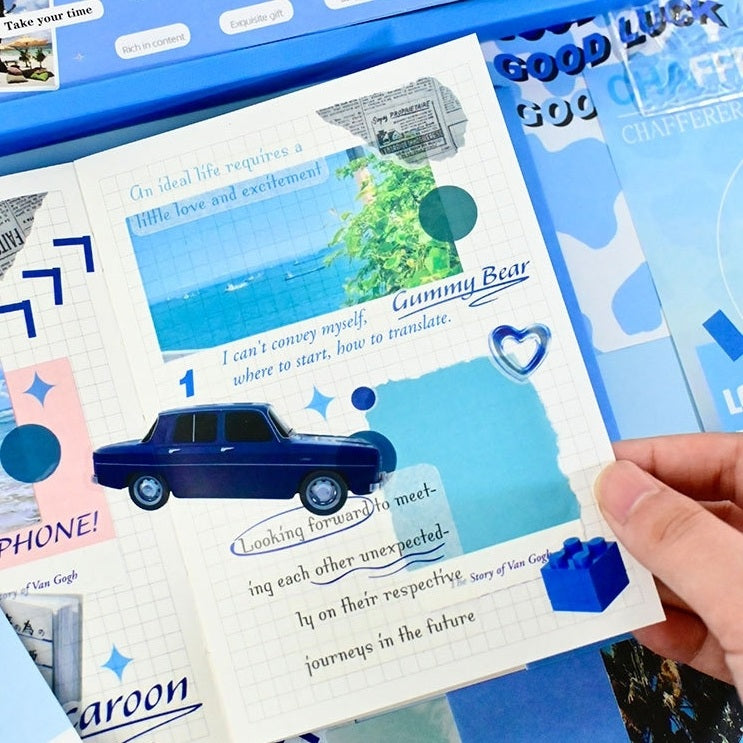 Hand holding a scrapbook with blue car illustration and text, surrounded by other cards with similar designs.