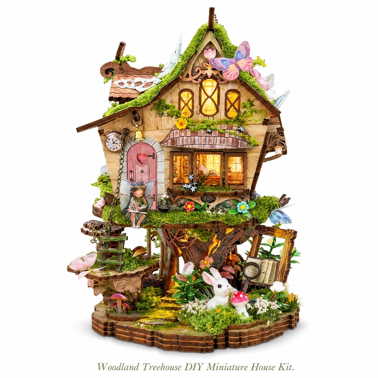 A woodland treehouse DIY miniature house kit displayed on a clean white background. The intricate fairy-tale style house features a mossy green roof, warm glowing windows, a pink fairy door, a small garden, mushrooms, butterflies, and a white rabbit figure on the base.