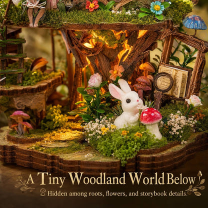 A miniature fairy garden scene with a white rabbit figurine beside a red mushroom, surrounded by moss, flowers, tiny trees, a small bridge, and warm fairy lights. Text at the bottom reads 'A Tiny Woodland World Below' with a small hidden-garden icon.